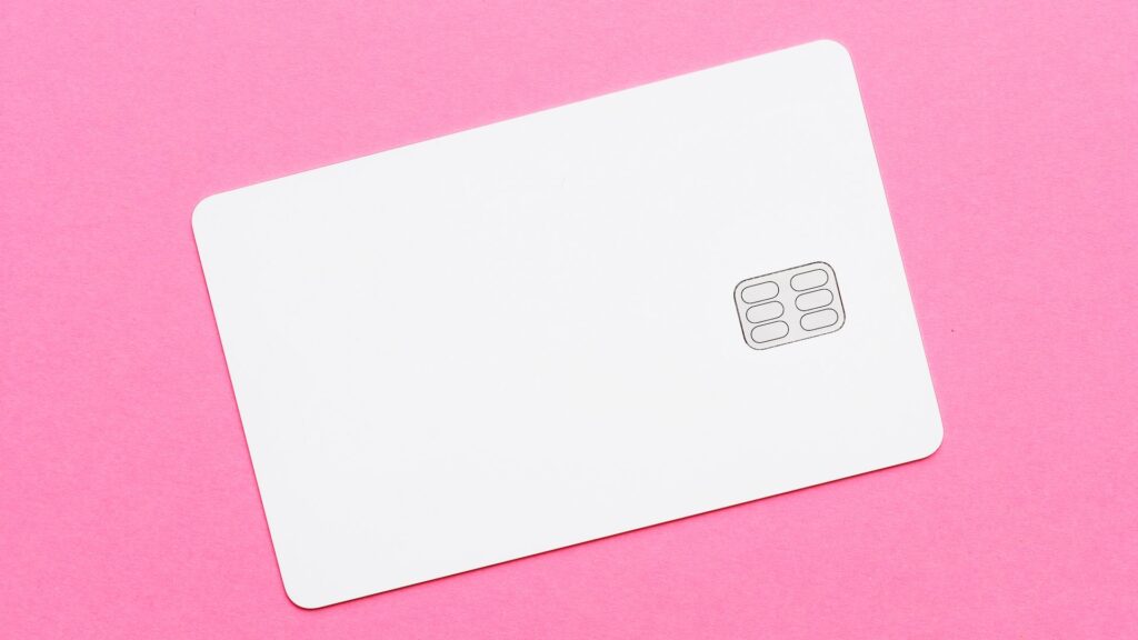 Белая банковская карточка лежит на розовой поверхности