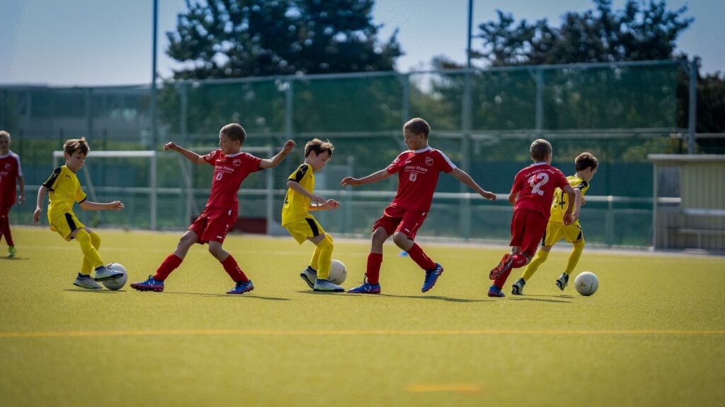 Мальчики в красной и желтой формах играют футбол на поле