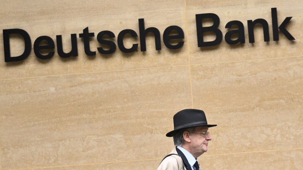 Логотип Deutsche Bank на стене, а мимо проходит человек в шляпе 