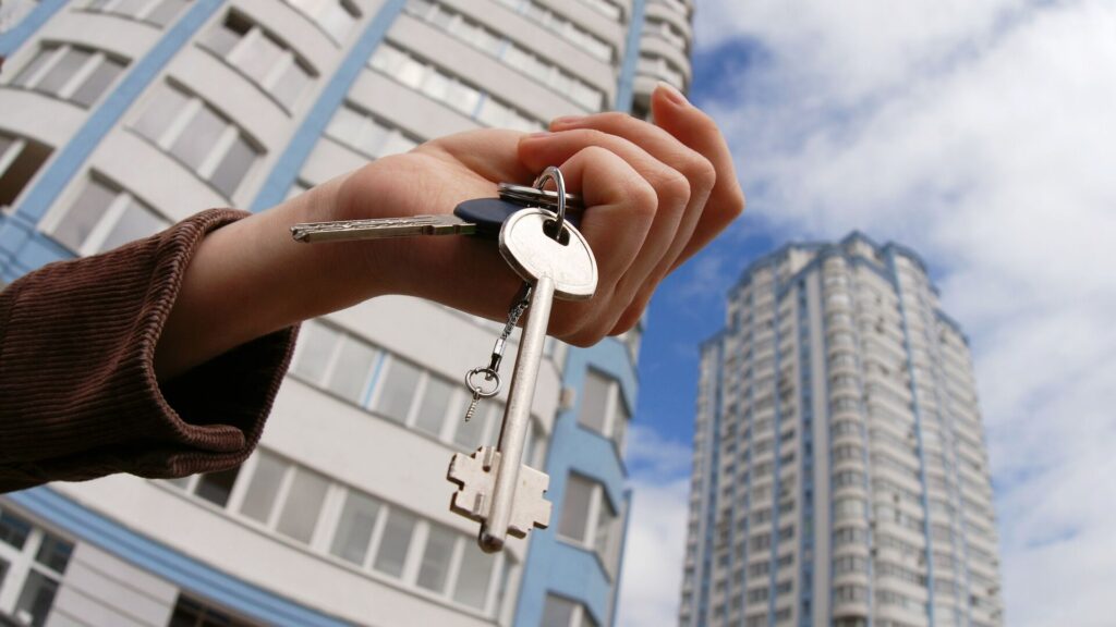 Человек держит ключи от квартире на фоне многоэтажки