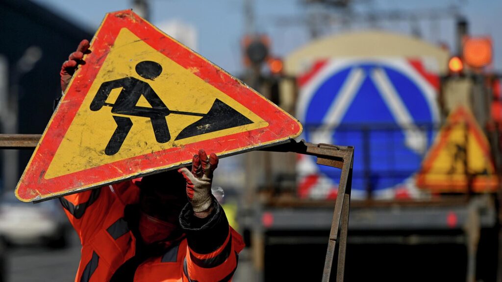 Рабочий ставит знак ремонта дороги