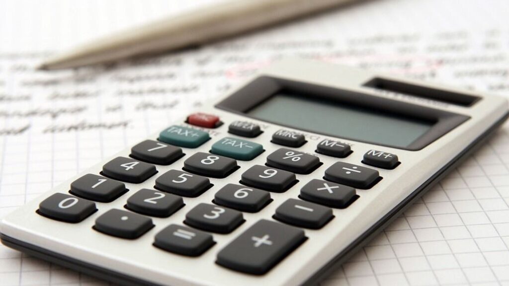 Калькулятор лежит на столе рядом с ручкой и счетами