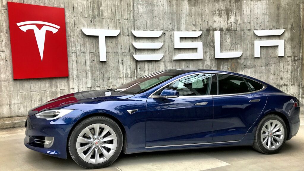 Автомобиль Tesla и на фоне логотипа компании