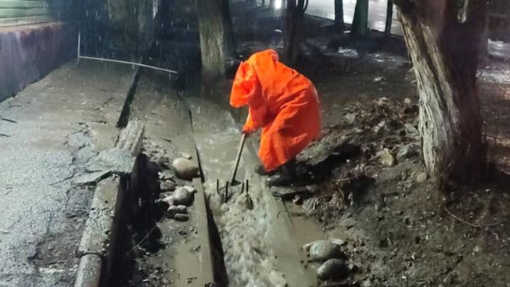 Человек чистит арык в Алматы под проливным дождем