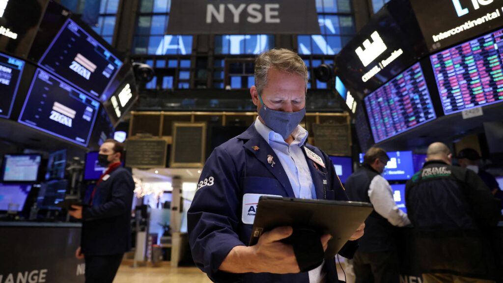 Трейдер в маске на лице работает на торговой площадке Нью-Йоркской фондовой биржи (NYSE) в Нью-Йорке.