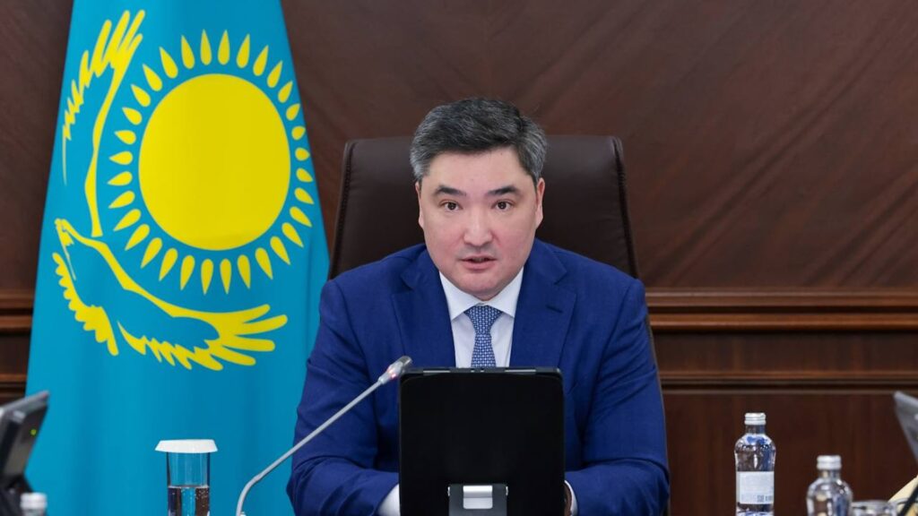 Бектенов на заседании правительства крупным планом на фоне флага Казахстана