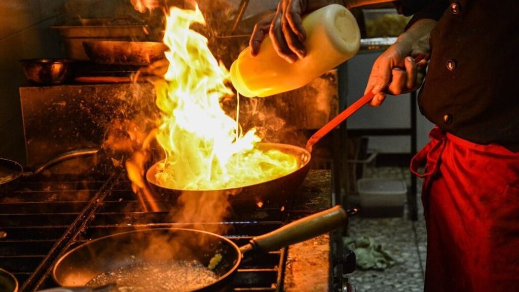 Повар добавляет масло в огонь на сковороде