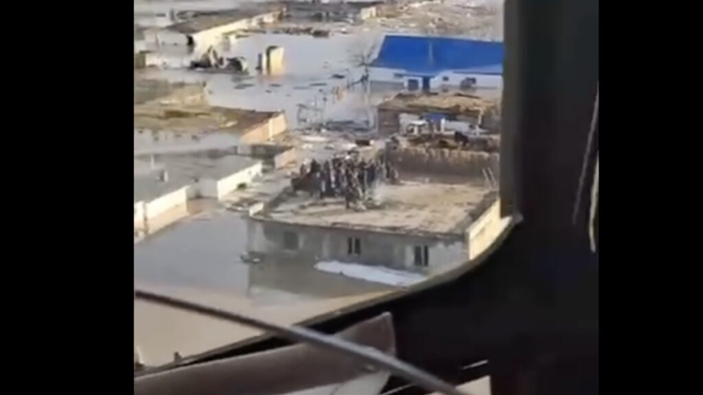 Люди стоят на крыше здания в ожидания вертолета для спасения от паводков