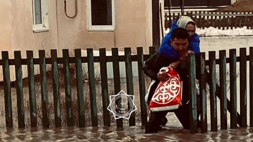 Сотрудник МЧС на спине несет женщину через воду, которая затопила дом