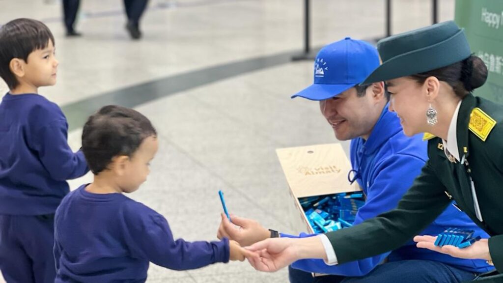 Двое взрослых дают детям бесплатный шоколад "Казахстанский" в аэропорту Алматы
