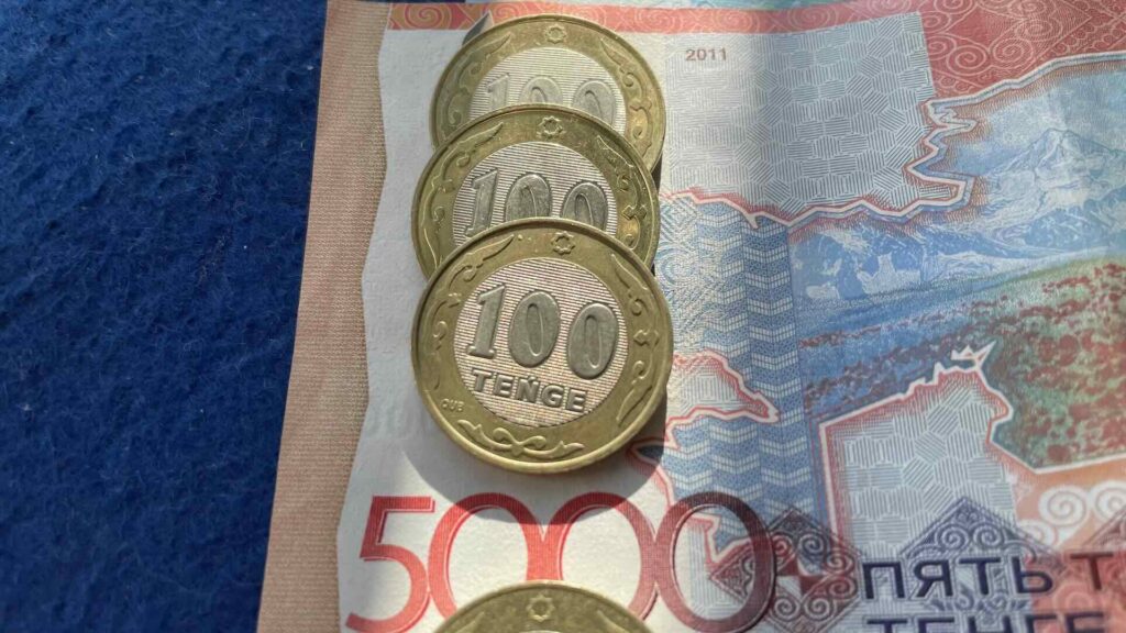 Четыре монеты по 100 тенге лежат сверху купюры в 500 тенге