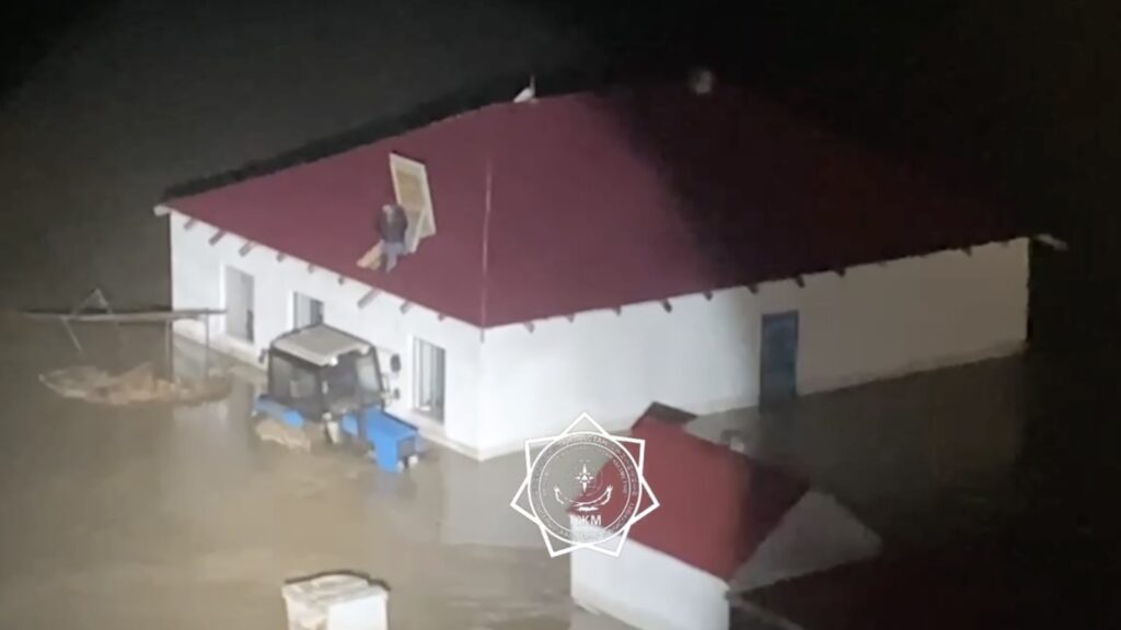 Человек стоит на крыше дома при затопленном доме и тракторе в Костанайской области