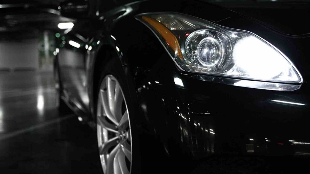Включенный фары светят в темном помещнии на черном автомобиле