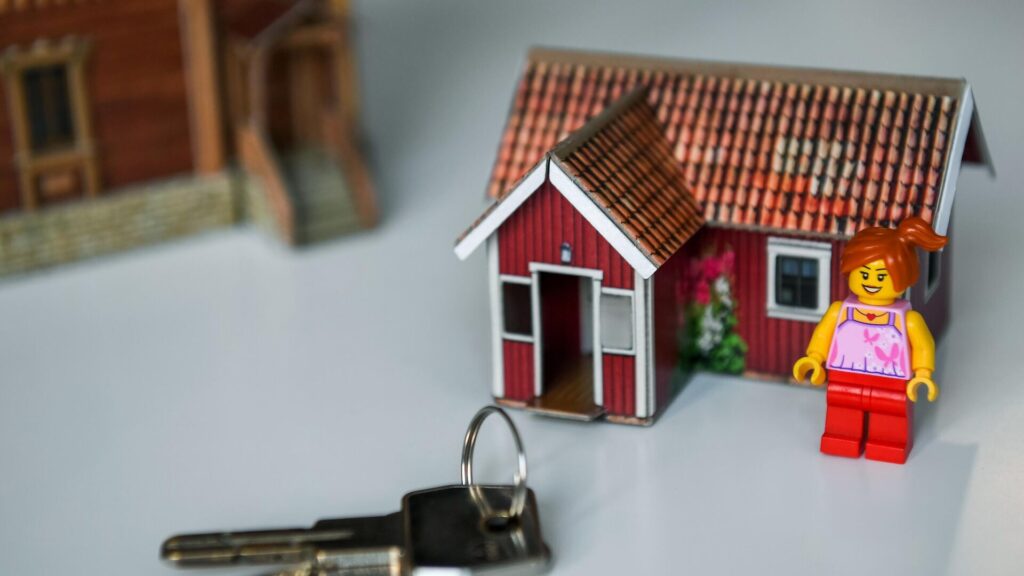Модель дома, ключи и фигурка Лего стоят на столе