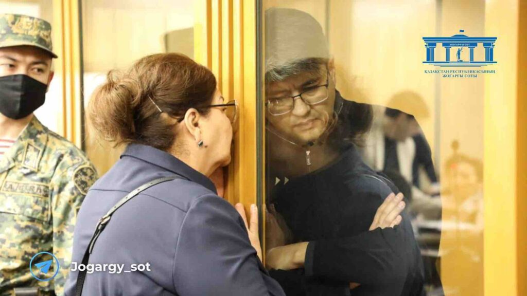 Куандык Бишимбаев слушает свою мать через стекло в зале суда