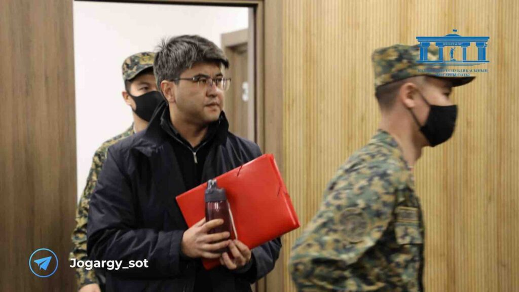 Куандык Бишимбаев с красной папкой идет за военным в зале суда