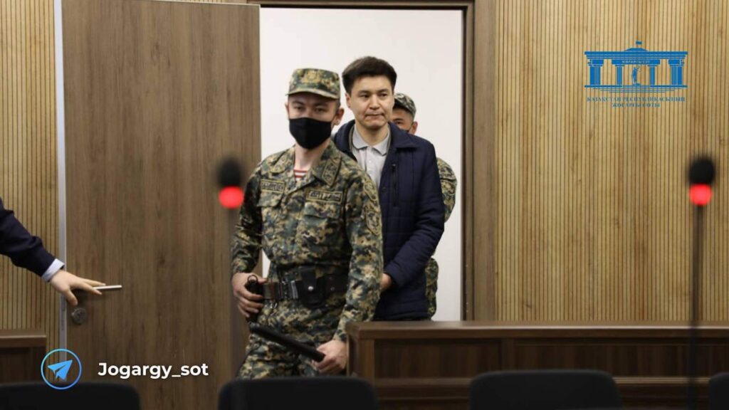 Бахытжан Байжанов идет рядом с конвоиром в зале суда