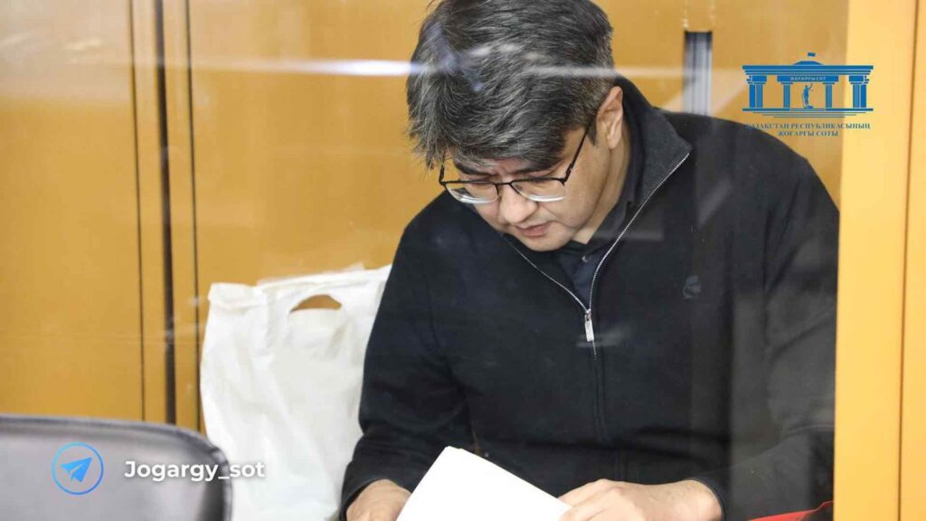 Куандык Бишимбаев опустив голову читает лист бумаги
