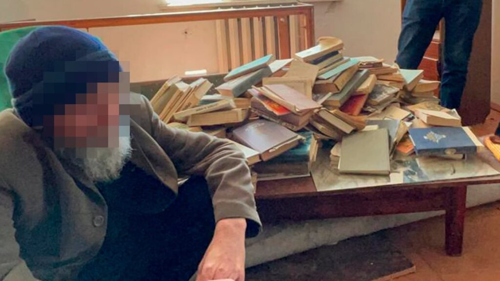 Задержанный экстремист в Казахстане сидит на полу рядом со столом, на котором экстремистская литература