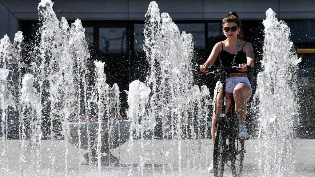 Девушка едет на велосипеде через струи фонтана