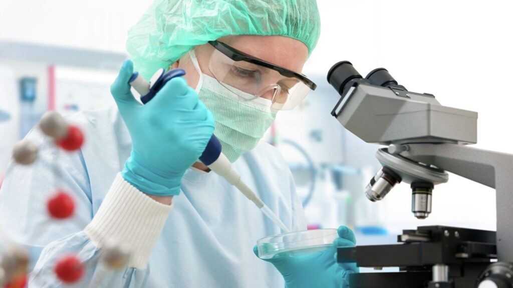Лаборант изучает анализы в маске и очках под микроскопом