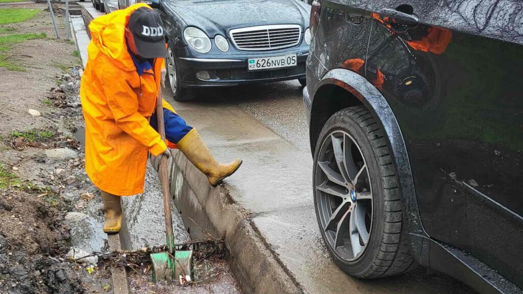 Человек чистит арык в Алматы после проливного дождя