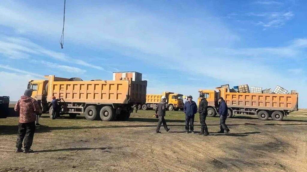 Мужчины стоят на фоне грузовиков в поле, где буду строить дома для пострадавших то паводков в Костанайской области