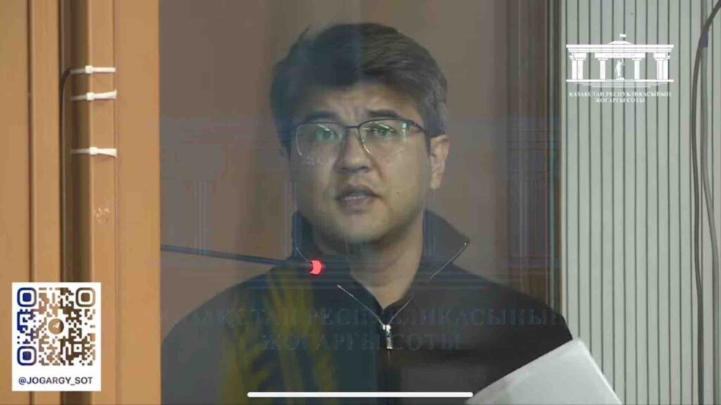 Куандык Бишимбаев с листком бумаги говорит в микрофон во время судебных прений