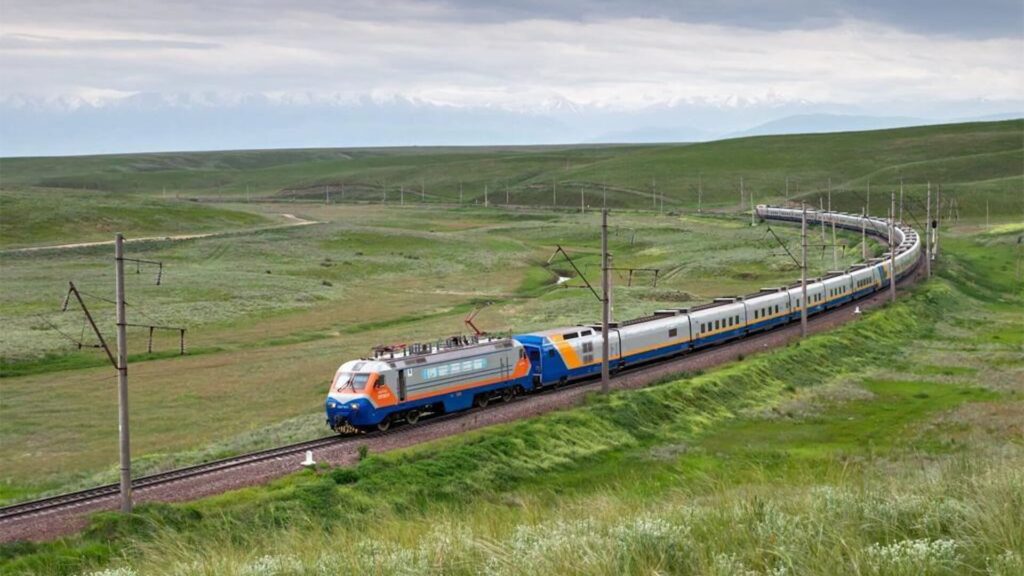 Поезд едет на железнодорожным путям в степи Казахстана