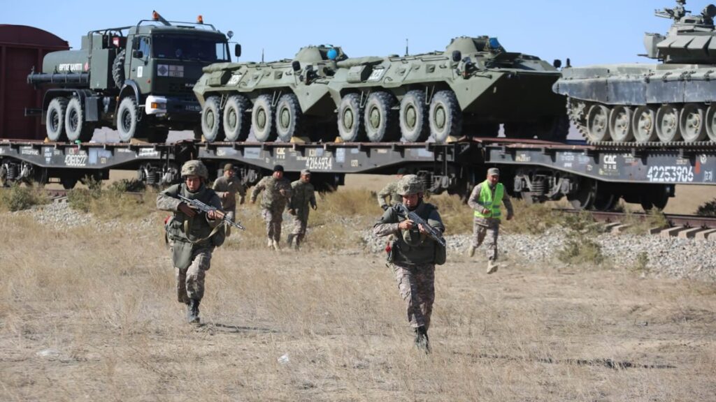 Военные бегут на фоне техники, перевозимой на поезде