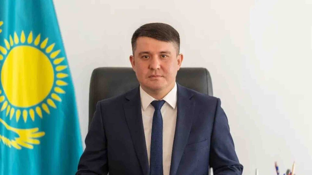 Думан Рахметкалиев в костюме рядом с флагом Казахстана