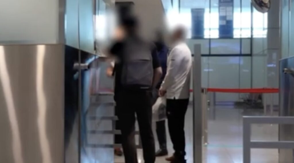 Экстрадированный преступник стоит в аэропорту в окружении полиции