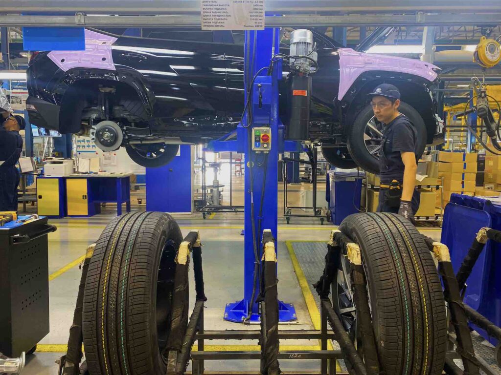 Работник завода устанавливает колеса на почти собранный автомобиль